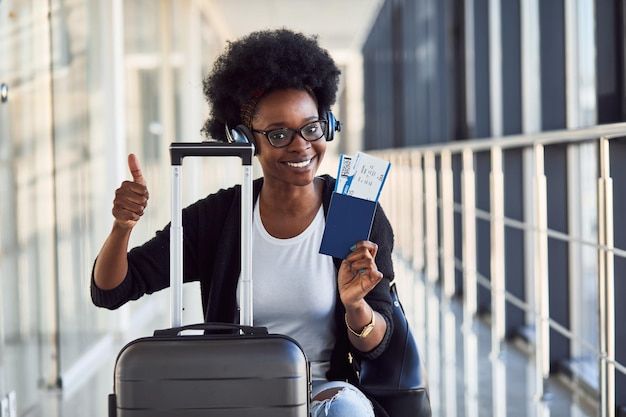 Premium Photo _ Young african american female passanger in casual clothes and headphones is in airport with baggage_