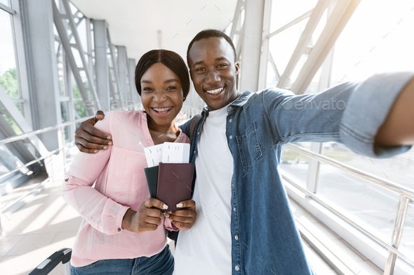 Traveling Together_ Happy african couple taking selfie in airport, waiting for boarding